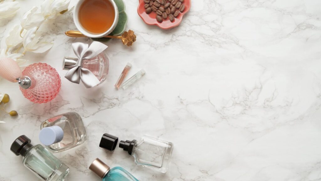 Uma bancada de mármore com vários frascos de perfume, flores e uma xícara de chá.
